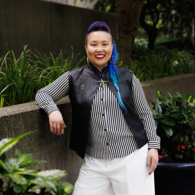 Kimfer wearing a black and white striped shirt and white pants while standing outdoors.