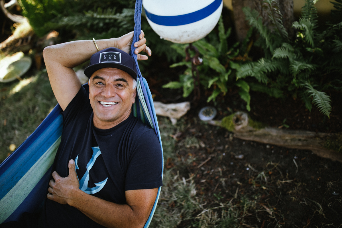 Felipe reclines in a bright blue hammock, smiling warmly up at the camera. Below him, lush green grass fills the background, creating a relaxed, cheerful scene.