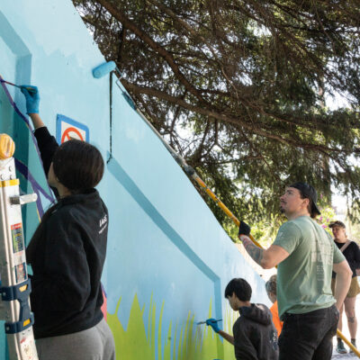 multiple volunteers working on the underpass painting with roller brushes and ladders.